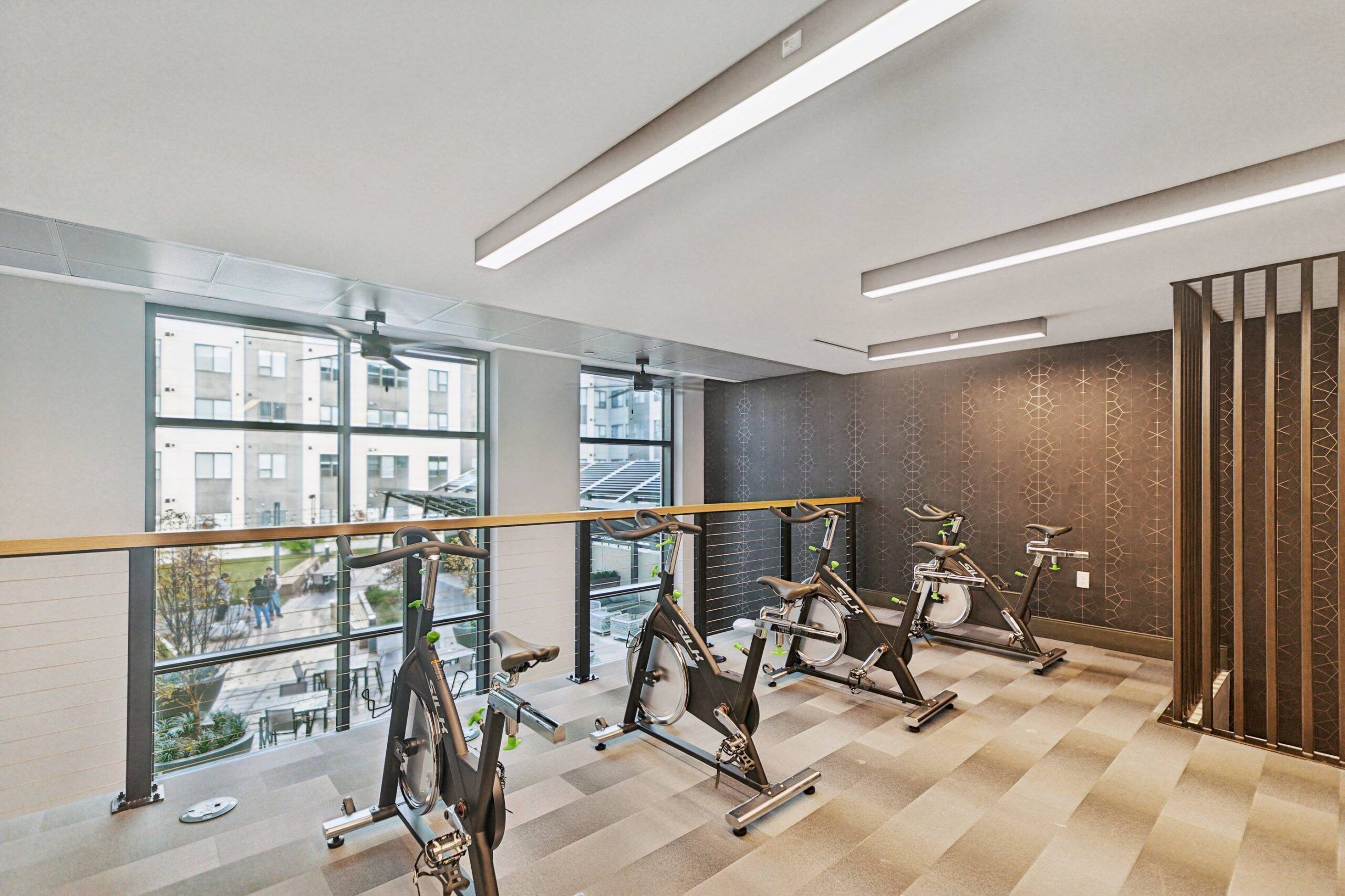 The Main On University features an indoor gym with stationary bikes, a patterned floor, large windows, and modern lighting.