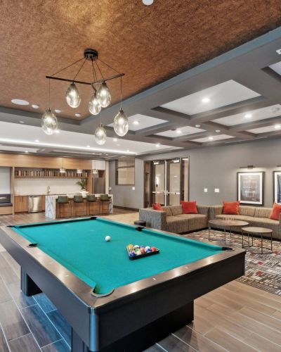 Modern game room at The Main On University with a pool table, foosball, gray sofas, stylish lighting, and a patterned carpet.
