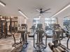 The Main On University features a modern gym with treadmills, ellipticals, weights, large windows, and ceiling fans on a gray checkered floor.