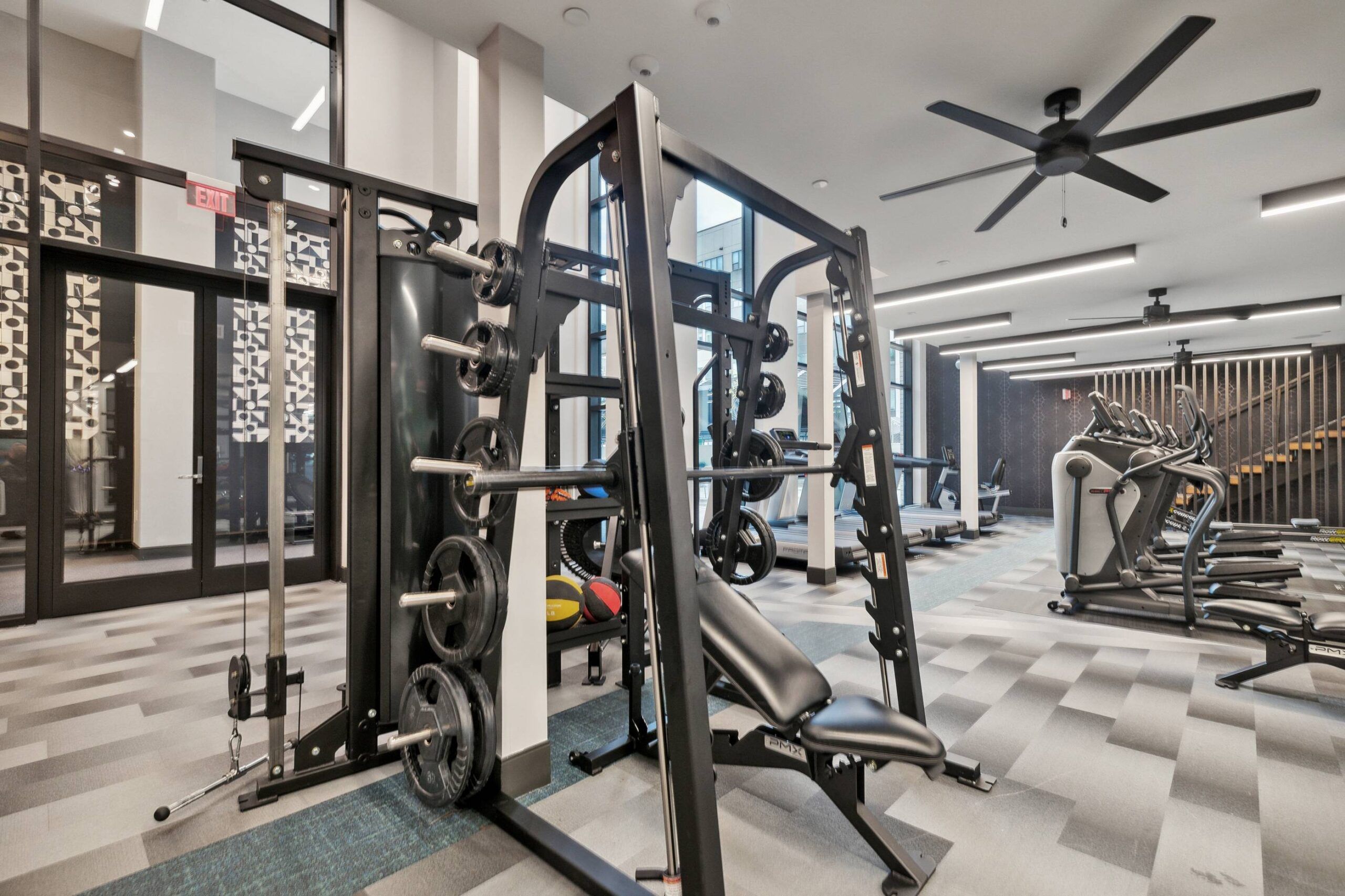 The Main On University offers a modern gym with weight machines, treadmills, and exercise equipment on a carpeted floor, ceiling fans above.